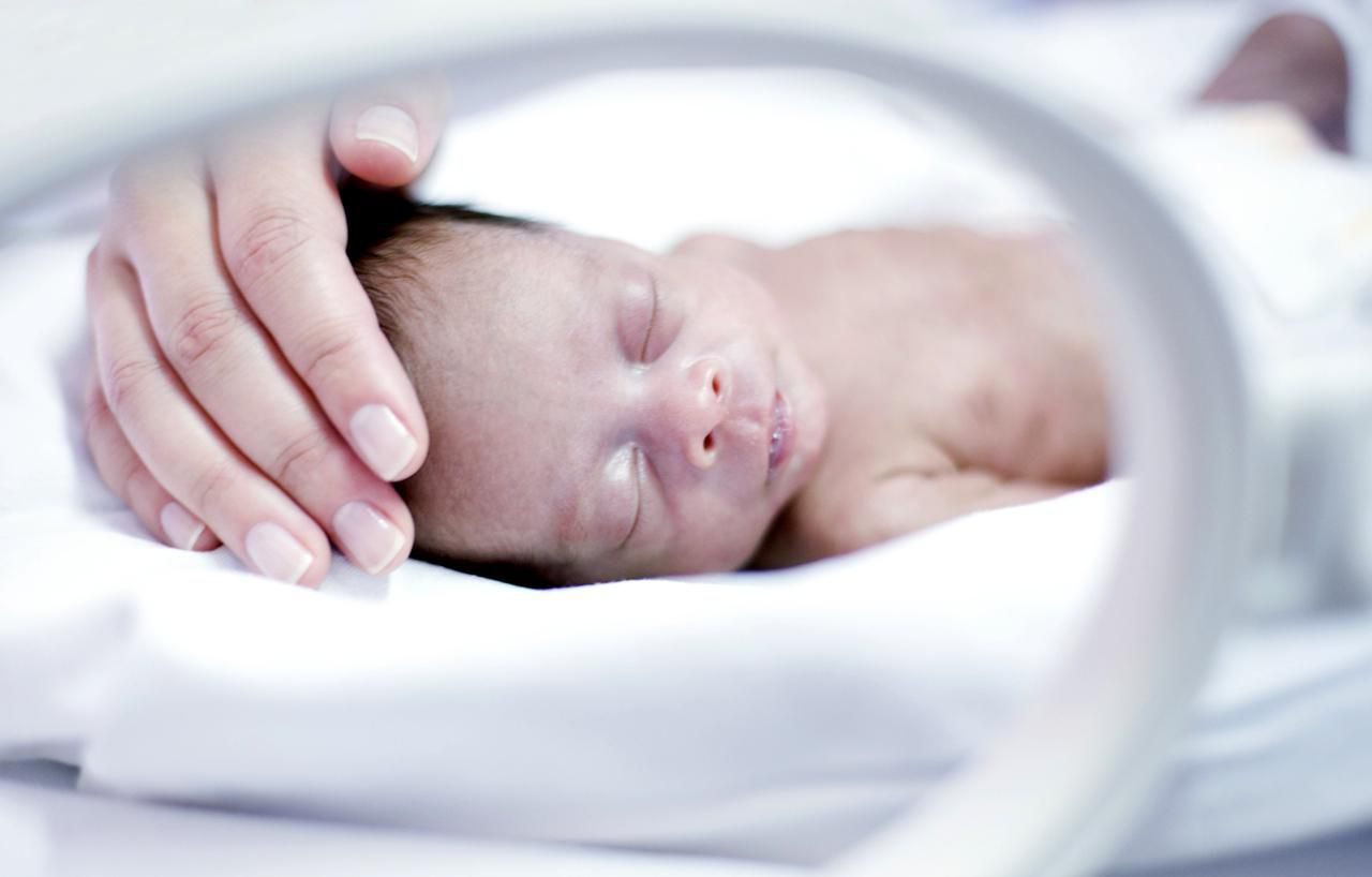 Adult hand gently stroking a mico preemie in an incubator 