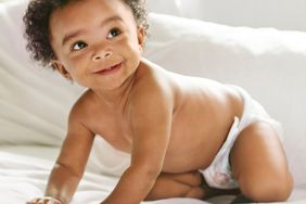 baby with curly hair crawling on bed