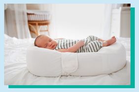 Baby sleeping on a positioner on a bed.