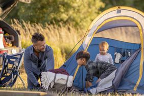 A small family is seen setting up their tent as they settle in to camp. 