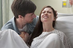 Man supporting a woman as she delivers a baby