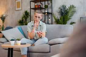 A woman with short hair sitting on her couch looking at a pregnancy test