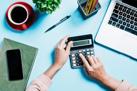 An image of a woman using a calculator at a desk.