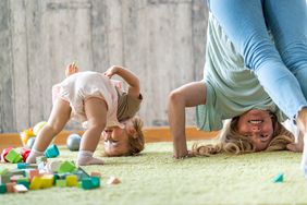 mom and toddler daughter playing on the green carpet with toy blocks scattered around