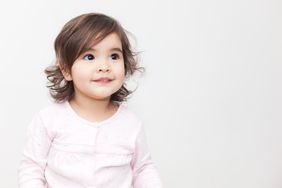 Brunette toddler girl in a pink shirt with a white background. 