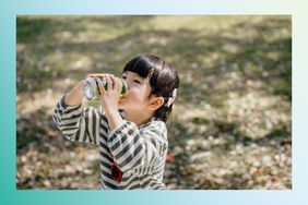 Little Asian girl drinking soda from can on a sunny day outdoors in the park 