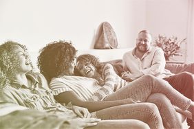 Laughing daughter embracing mother while sitting on couch with family in living room