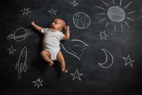 baby lying on a chalk board with planets and suns drawn on