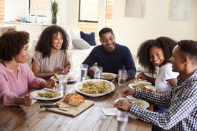 black couple sitting at dinner table eating and talking with with their teen children