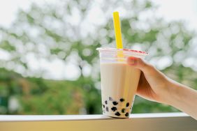 Human hand holding a cup of iced cold bubble tea with milk and tapioca pearls