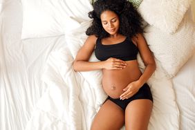 High angle view Of pregnant Black woman lying on bed holding her belly