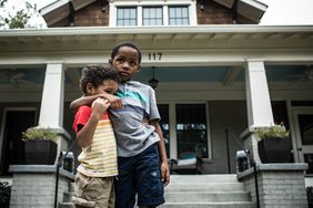 Two boys embrace while standing in front of a house