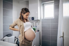 One woman, pregnant lay standing alone and in pain in bathroom.