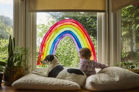 baby sitting with dog in front of window with rainbow decal