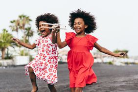 Twins sisters running on the beach while playing with wood toy airplane 