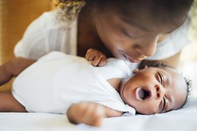 Mother looking at newborn yawning while lying on bed