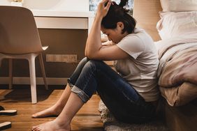 Asian woman sitting on floor next to bed feeling depressed