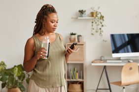 Black person looking at phone and drinking water from a bottle