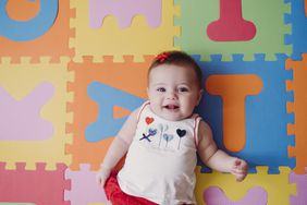 Smiling baby girl wearing a red bow laying on a colorful play mat