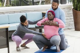 A pregnant African-American woman with her husband and her doula or birth support coach. She is practicing squatting.