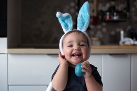 Cheerful Laughing Baby Wearing Blue Bunny Ears And Holding Blue Easter Egg