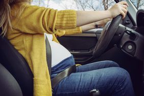 Pregnant woman fastening safety belt in car