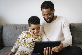 Father and toddler son watch a tablet on the couch