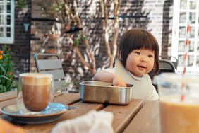 Baby Girl eating out of a lunch box at an outside restaurant