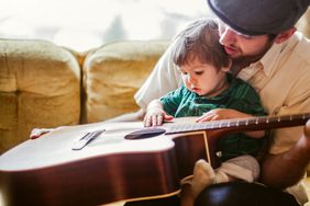 baby sitting with parent and holding an acoustic guitar