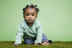 baby in green shirt sitting on grass with green background