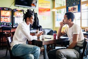 A couple of stylish friends sitting down together at a pool hall, talking and catching up while drinking coffee.