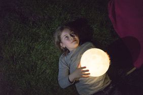 girl lying on a meadow holding a moon