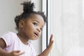 Toddler girl wearing pink t-shirt looking at a window