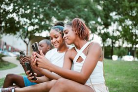 A group of Black teenage girls, share social media content on their smartphones in an outdoor setting