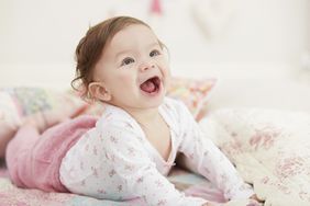 Baby girl in pink pants smiling on bed 