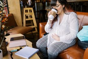 pregnant person holding stomach while drinking coffee