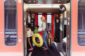 Mom and kids board a train with luggage for a trip.