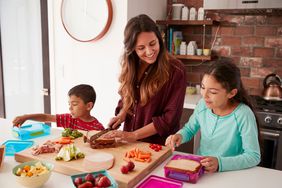 Children Helping Mother To Make School Lunches In Kitchen At Home