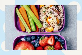 Overhead view of a lunch box filled with pasta salad, veggie sticks, and fruit.