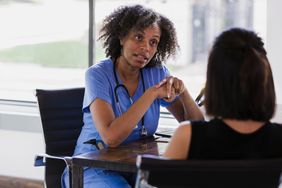 Female doctor speaks to patient from behind her desk