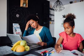 Mom applies for job at the kitchen table with her daughter sitting next to her. 