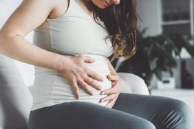 Pregnant woman sitting on the sofa holding her belly 