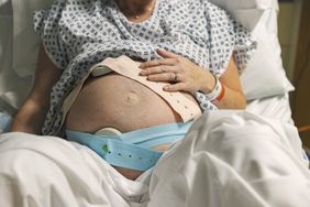 An unrecognisable mature pregnant woman lies on a hospital delivery bed as she has fetal monitoring.