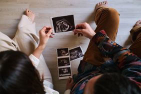 Couple sitting on the floor of their home look at their baby's ultrasound held by both of them.