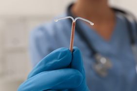 Doctor holding T-shaped intrauterine birth control device on blurred background