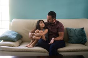 A little latin girl sitting with her father on the sofa at home and looking at him.