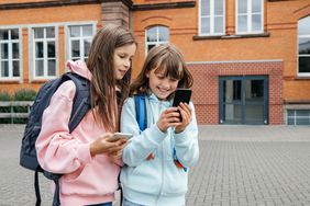 Kids looking at their phones while outside a school.