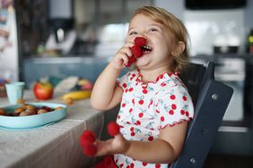 Young girl playing with raspberries on her fingers, in the kitchen