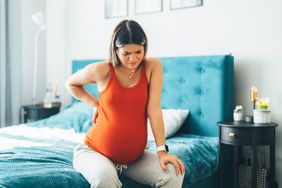 Pregnant woman feeling pain while sitting on bed