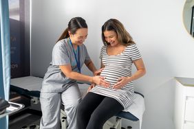 Friendly OBGYN gently presses on pregnant woman's abdominal. She is checking the fetal position. The pregnant woman is in her third trimester.